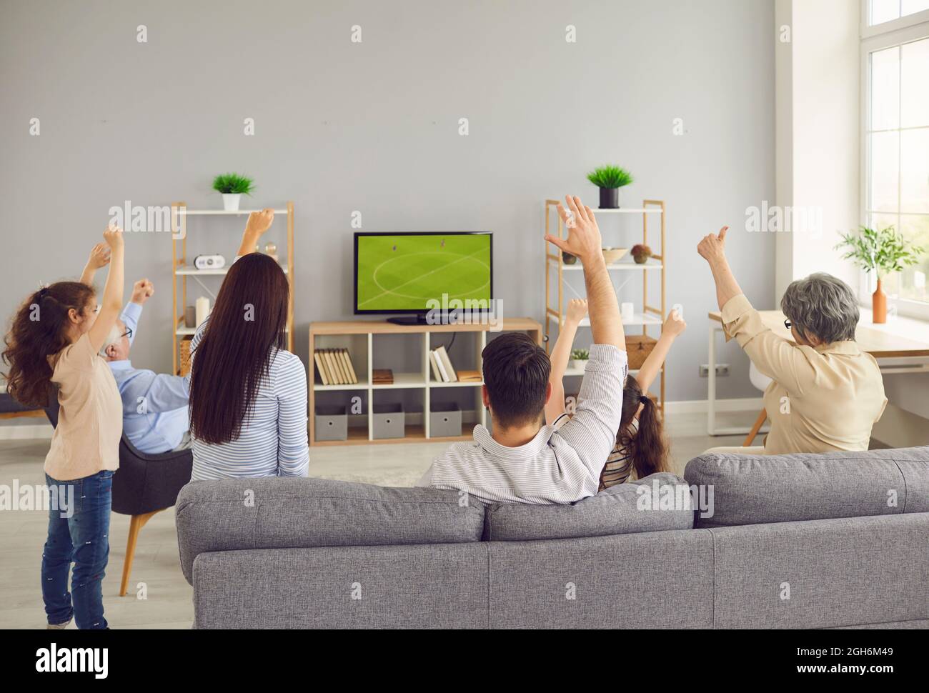 Back view of family sitting on sofa in living room and watching football match on TV Stock Photo