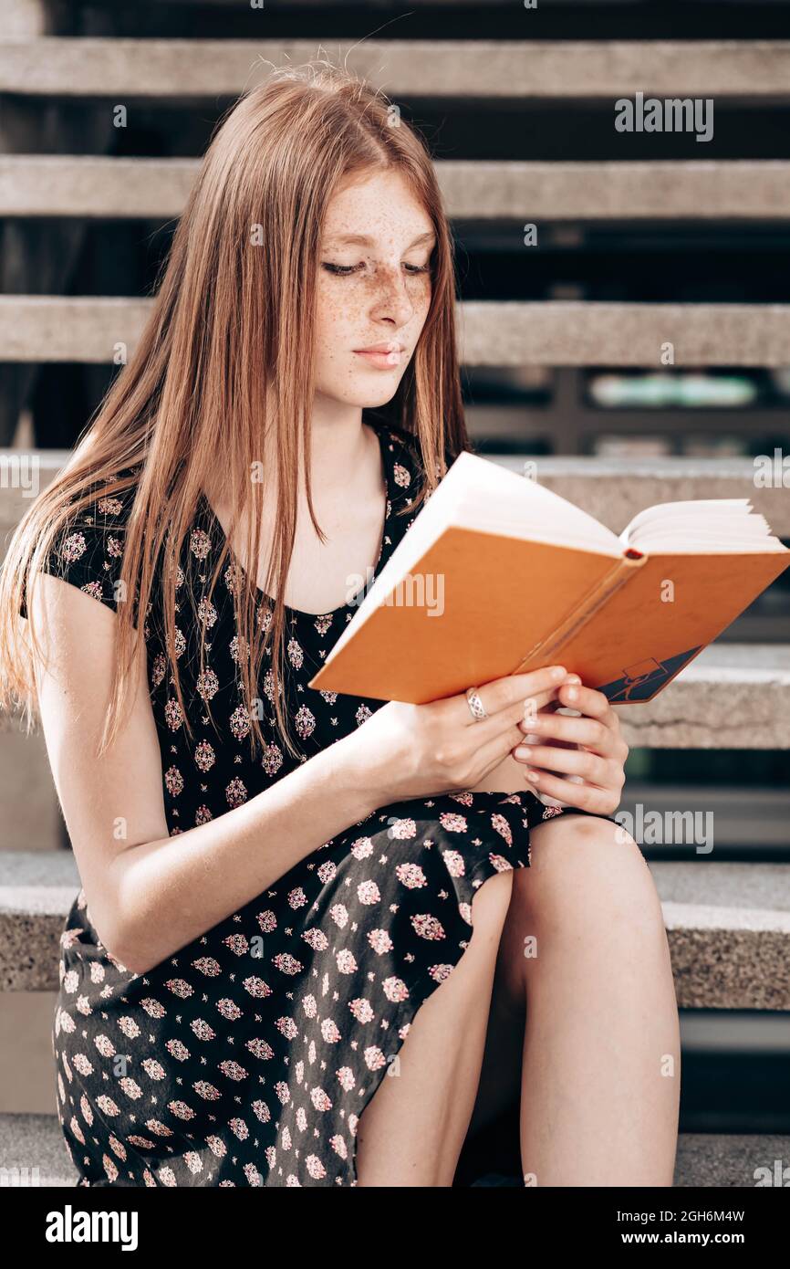 Young, ginger, teen school girl sitting on the stairs in front of her  school, reading a book Stock Photo - Alamy