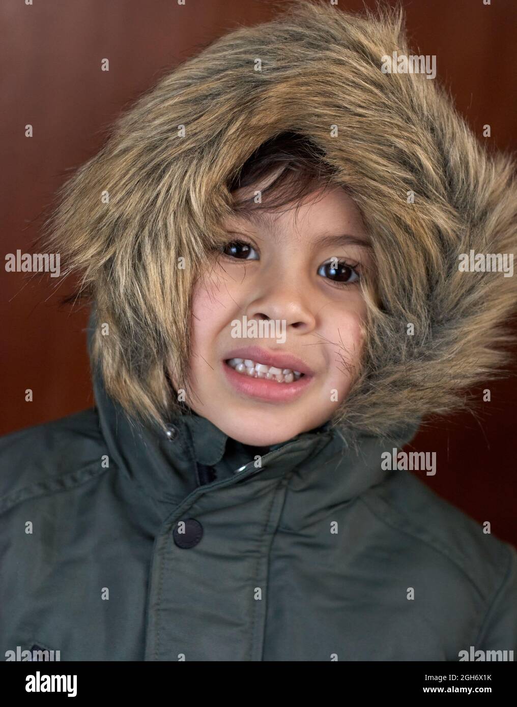 brunette scared boy in green overcoat parka against brown background. Vertical. Wintertime Stock Photo