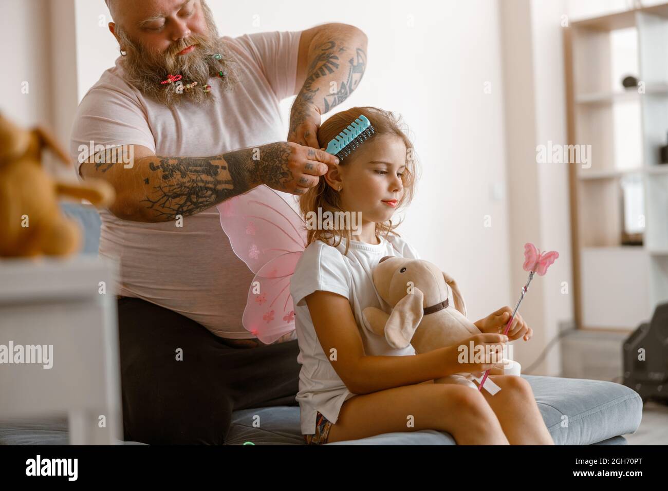 Daddy with scrunchies in beard brushes hair of cute little daughter at home Stock Photo