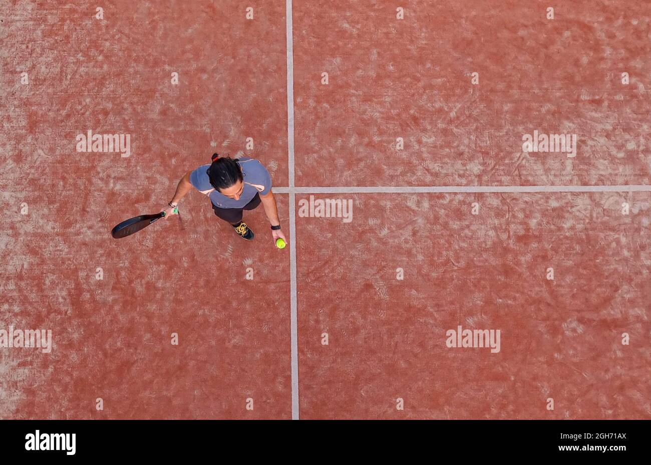 Top view of a paddle tennis player bouncing the ball for a serve on an outdoor court Stock Photo