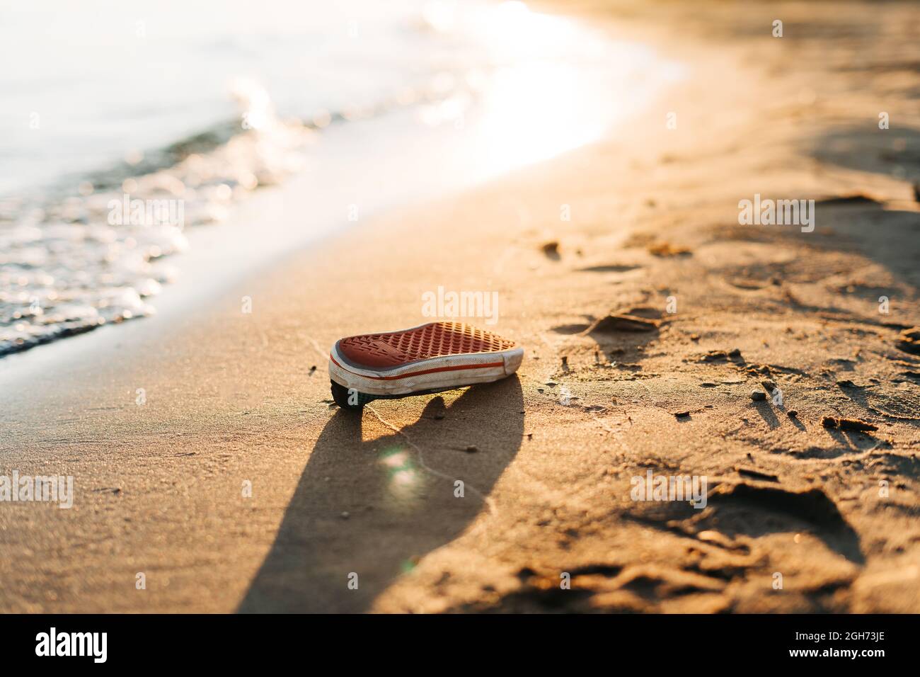 Used old shoe washed up on the shore of a beach, highlighting the worldwide crisis of garbage, plastic pollution. Environment ecology concept. Stock Photo