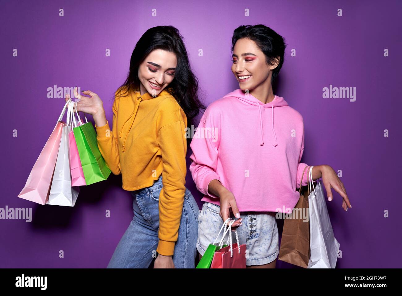 Two happy girls friends shoppers holding shopping bags on purple background. Stock Photo