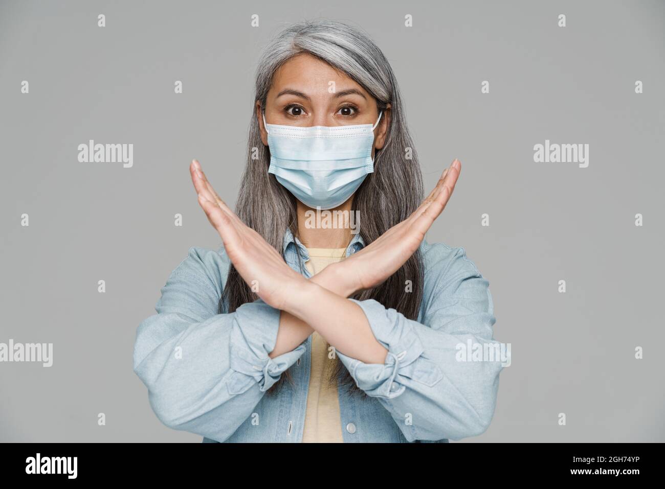 Mature white-haired woman in face mask showing stop gesture isolated ...