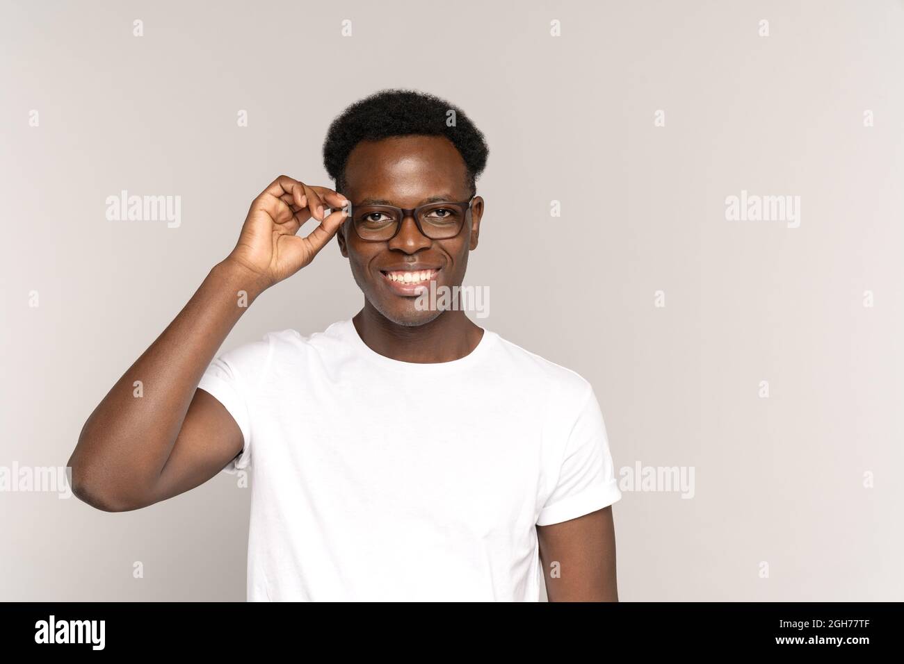 Young african guy with perfect toothy smile touch glasses wearing white t-shirt. Dentistry concept Stock Photo