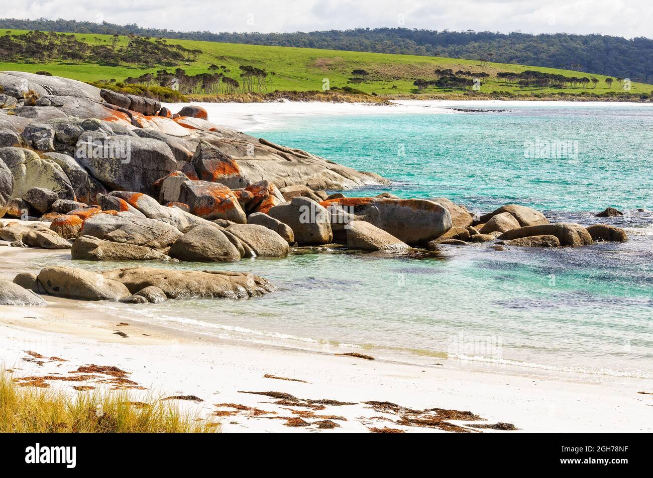 Orange lichen-covered granite boulders in a small white sandy beach - The Gardens, Tasmania, Australia Stock Photo