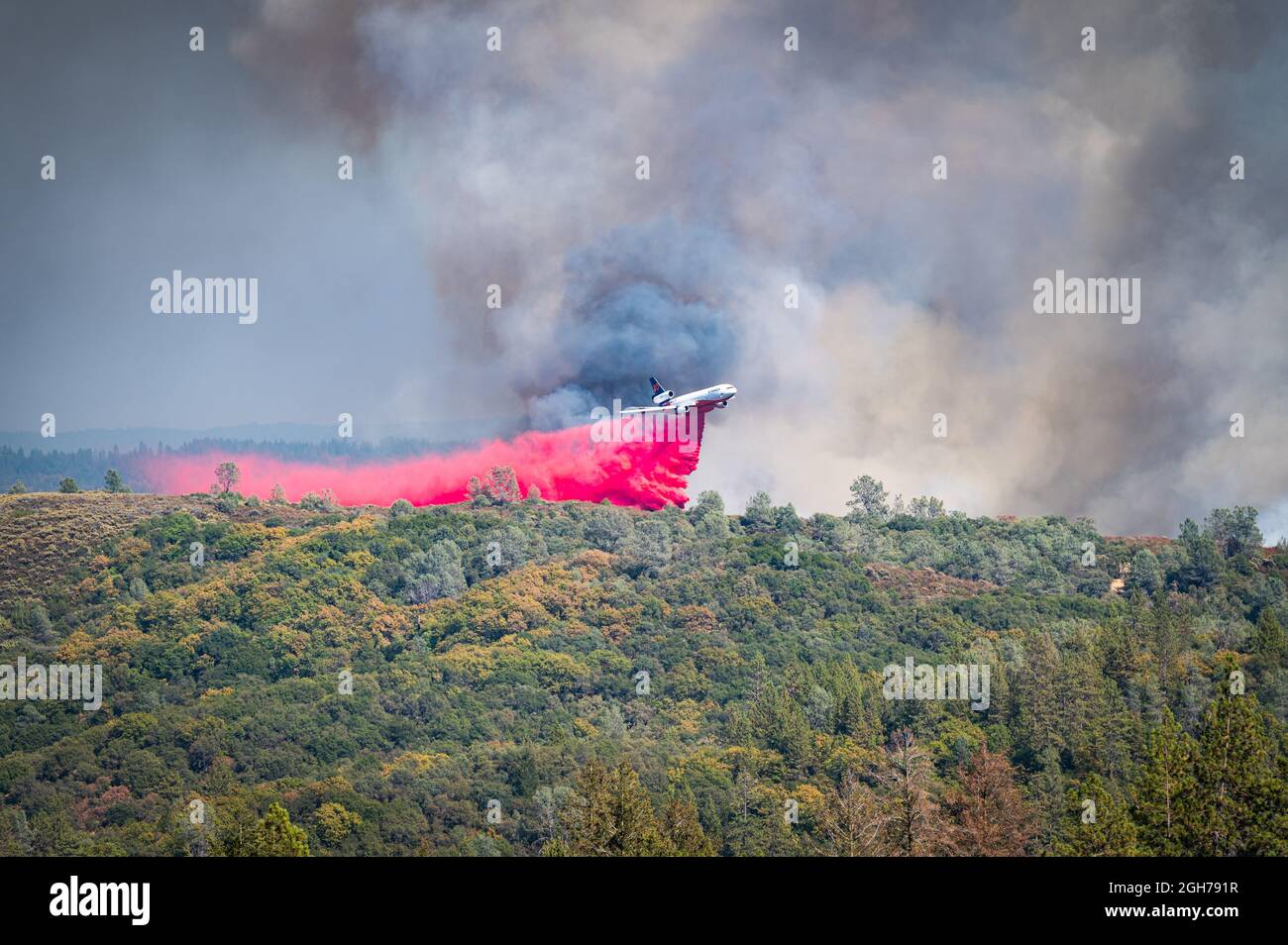 A Cal Fire plane drops bright red fire retardant on the Foresthill Bridge fire, near Auburn, California, in the Sierra Nevada foothills. Stock Photo