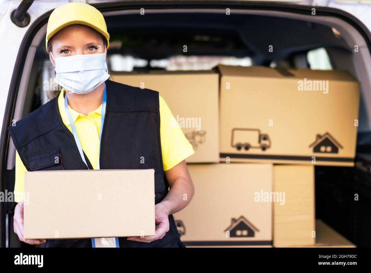 Health protection, safety and pandemic concept delivery woman in face protective medical mask holding parcel box. Copy space on the box. Stock Photo