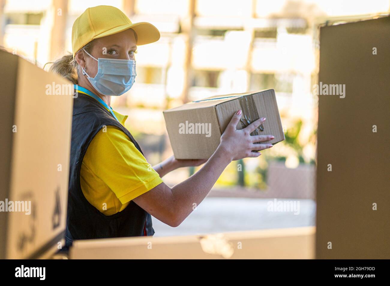 Health protection, safety and pandemic concept delivery woman in face protective medical mask holding parcel box. Stock Photo