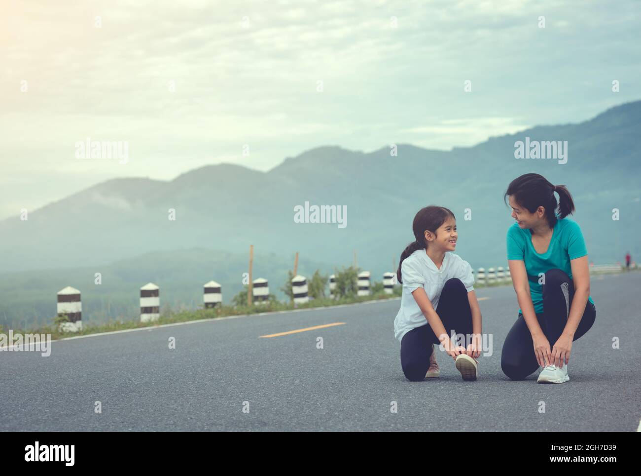 Mom and child are kneeling and tying shoelace. We getting ready for jogging outdoors the time during sunrise on dam road exercise. Stock Photo