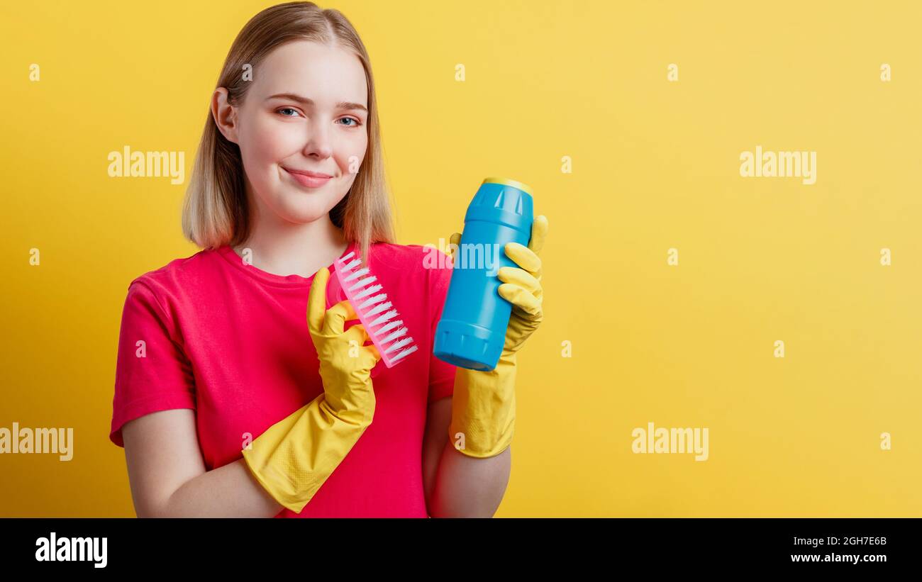 Young blonde happy smiling woman ready to cleaning house with household supplies isolated over yellow color background. Woman Portrait with cleaning Stock Photo