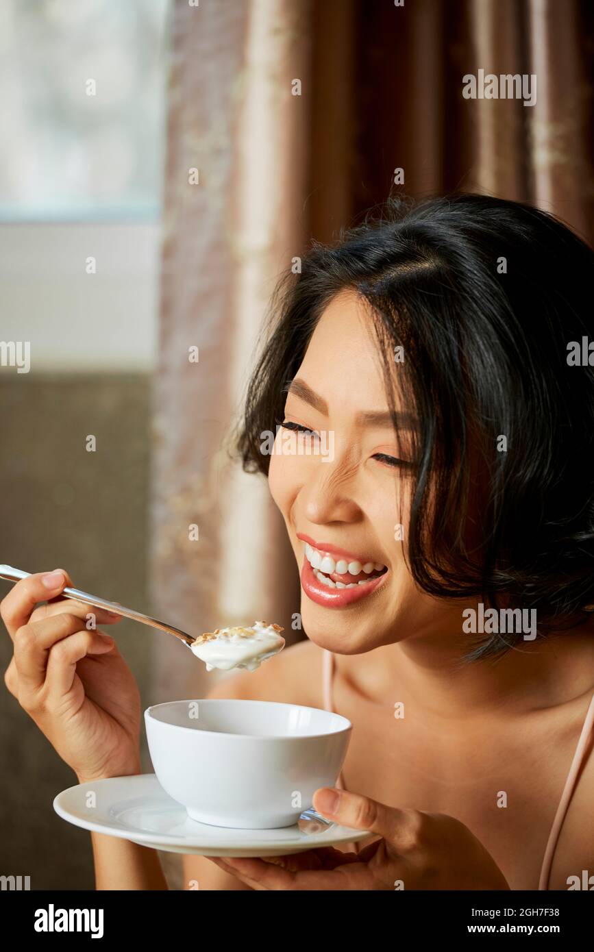 Joyful pretty young woman eating muesli with nondairy yogurt for