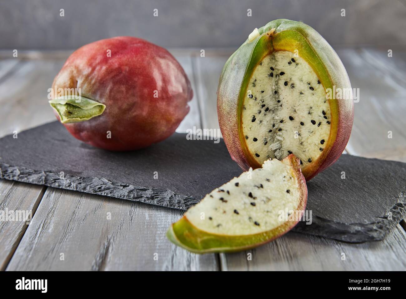 Peruvian apple cactus fruits whole and cut on wooden stand on gray board. Scientific name Cereus repandus Stock Photo