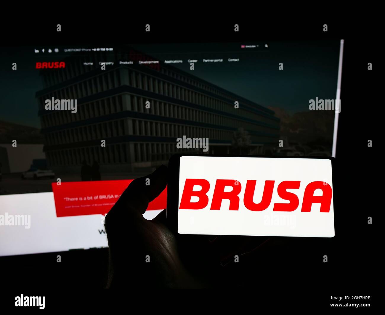 Person holding mobile phone with logo of Swiss electronics company BRUSA Elektronik AG on screen in front of web page. Focus on phone display. Stock Photo