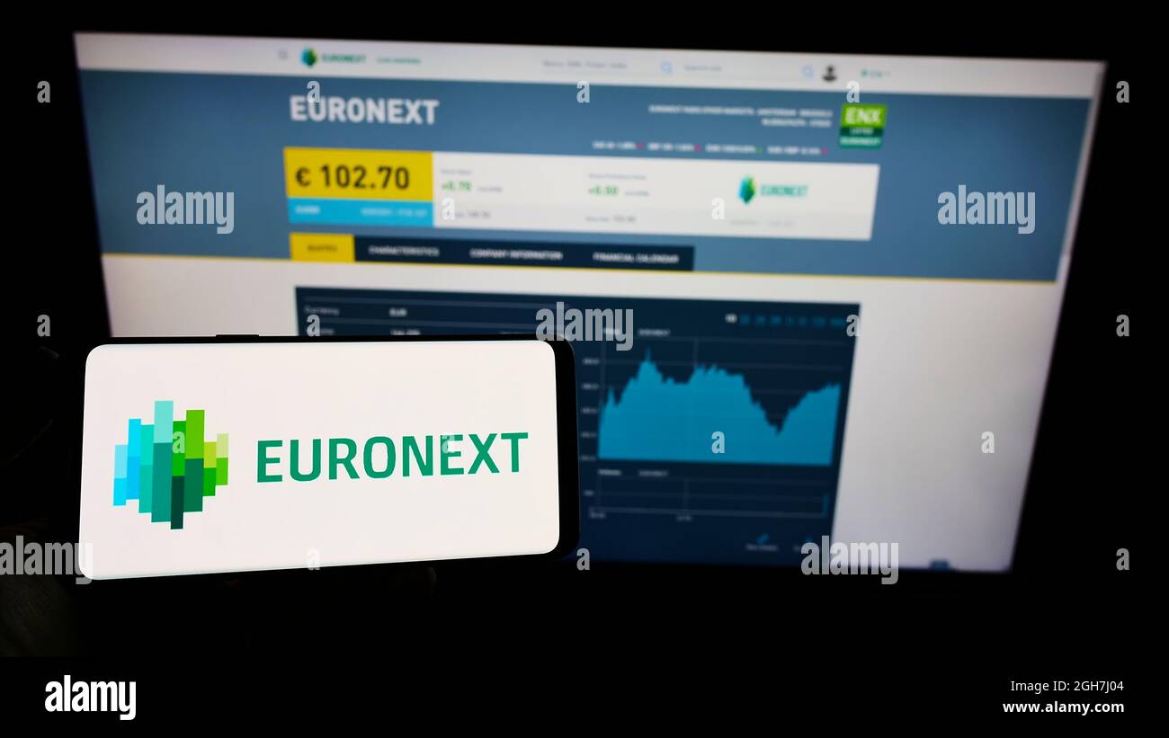 Person holding mobile phone with logo of financial services company Euronext N.V. on screen in front of business web page. Focus on phone display. Stock Photo