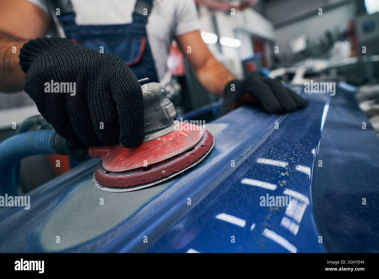 Repairman with sander removing old paint from car Stock Photo