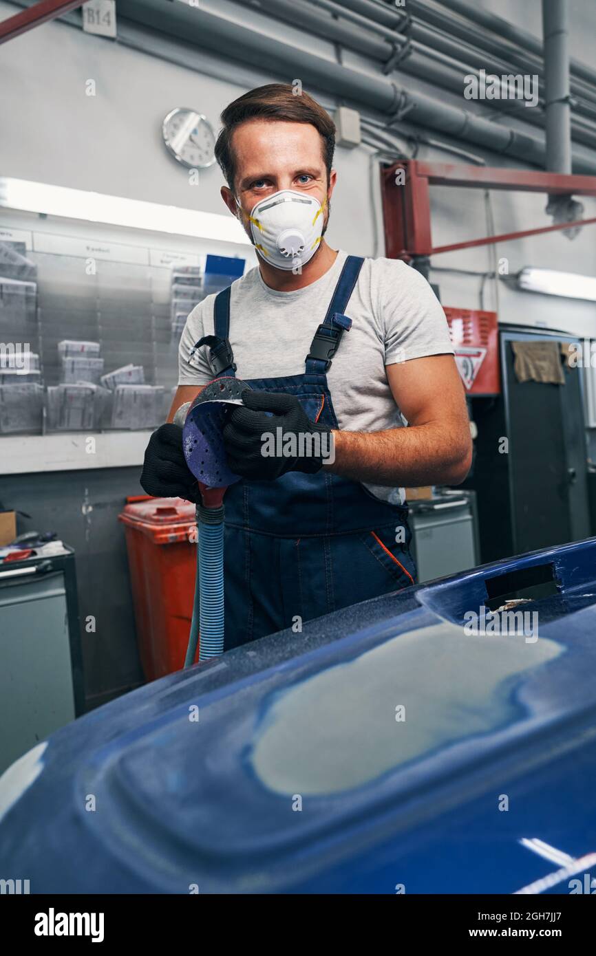 Glad automotive technician removing sandpaper from grinder Stock Photo