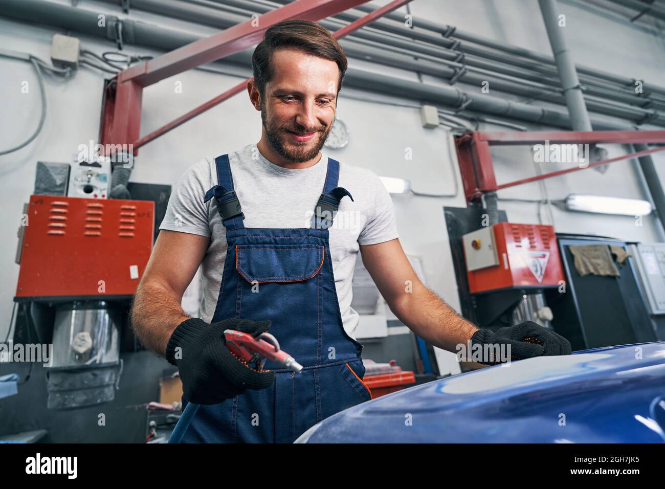 Satisfied mechanic using air gun for cleaning car part surface Stock Photo