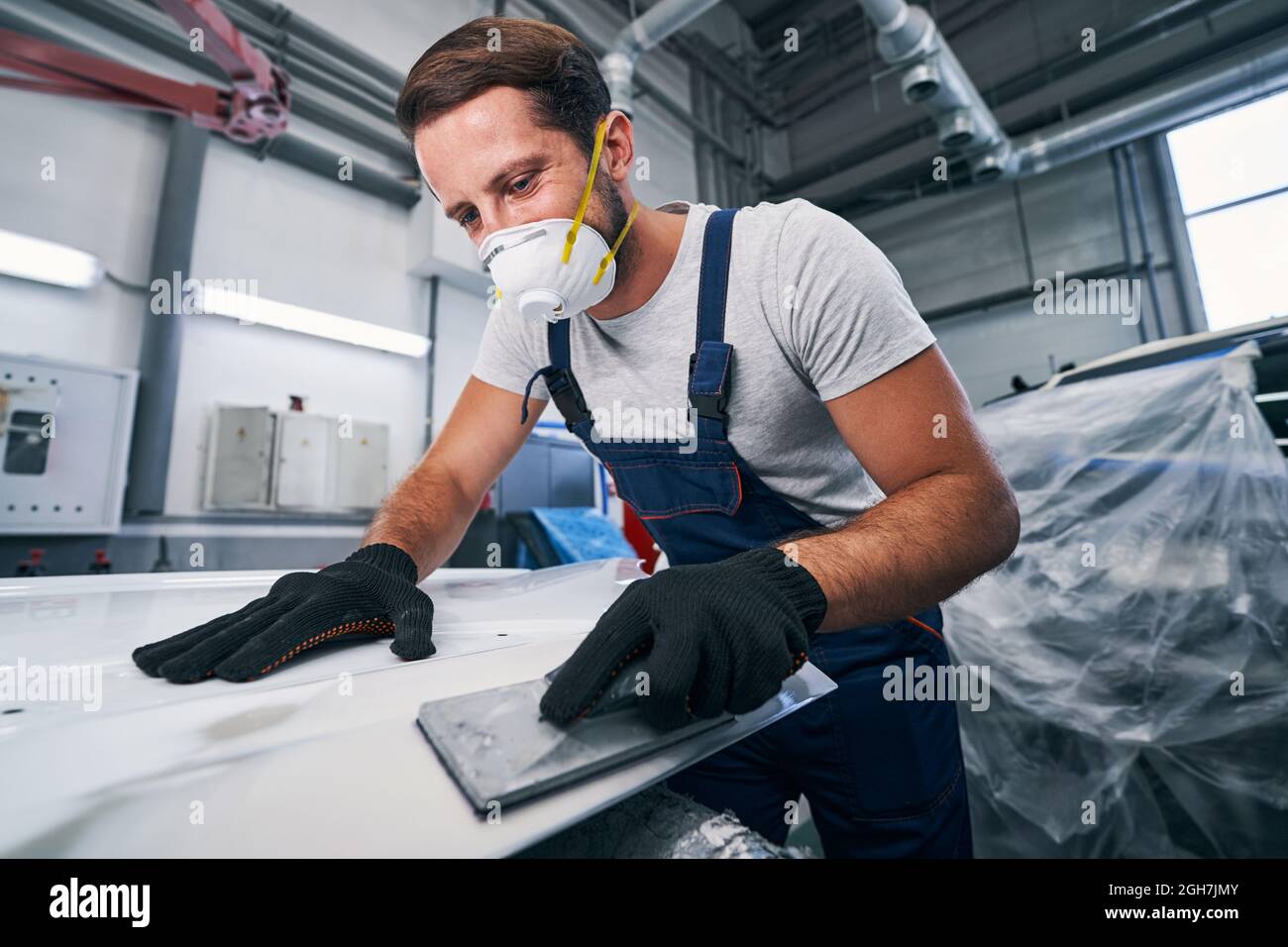 Man sanding white car part with hand instrument Stock Photo