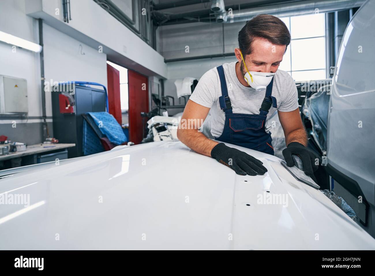 Optimistic car mechanic in process of manual car part sanding Stock Photo