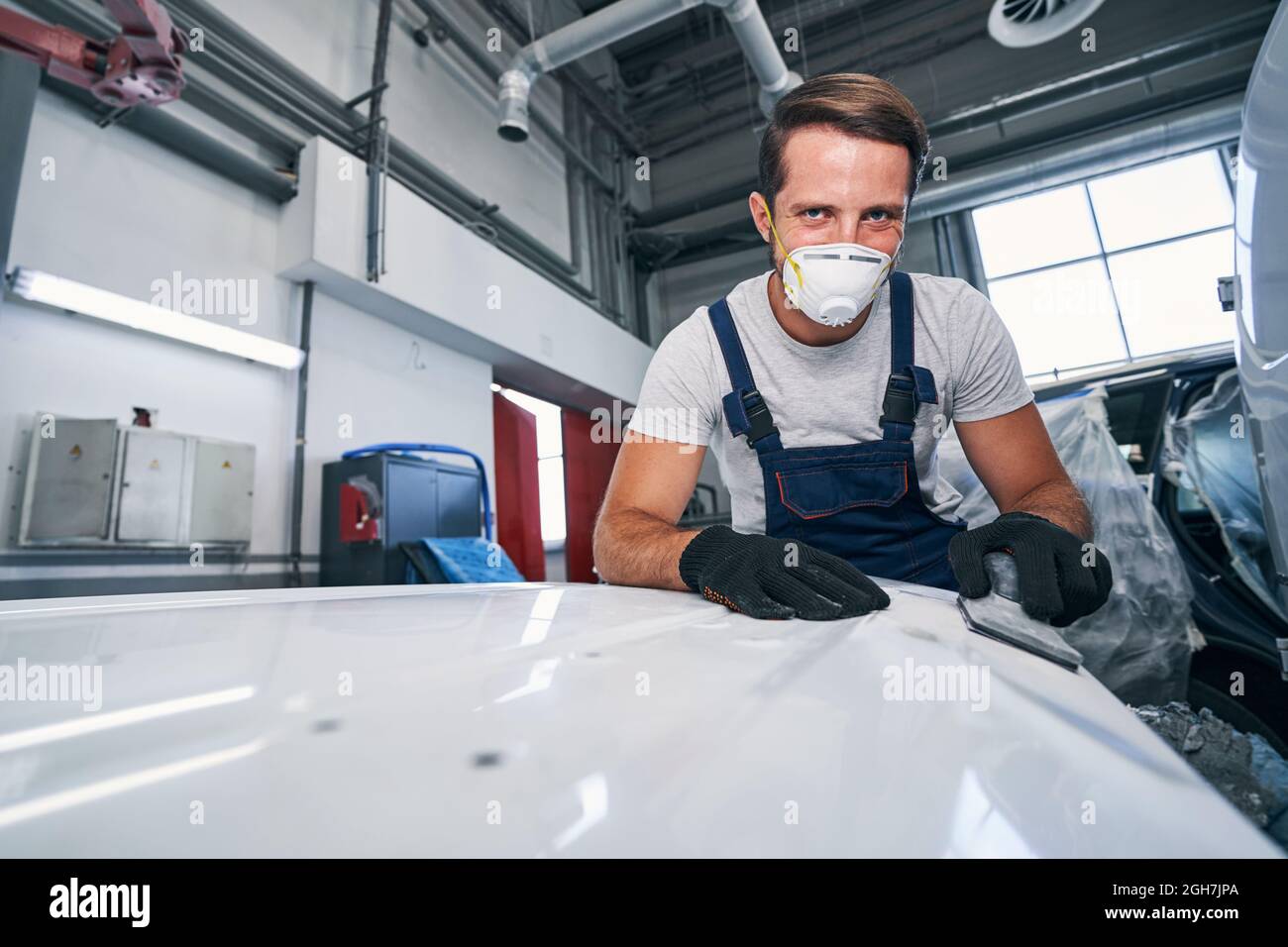 Cheerful auto technician leaning on car body part while sanding Stock Photo