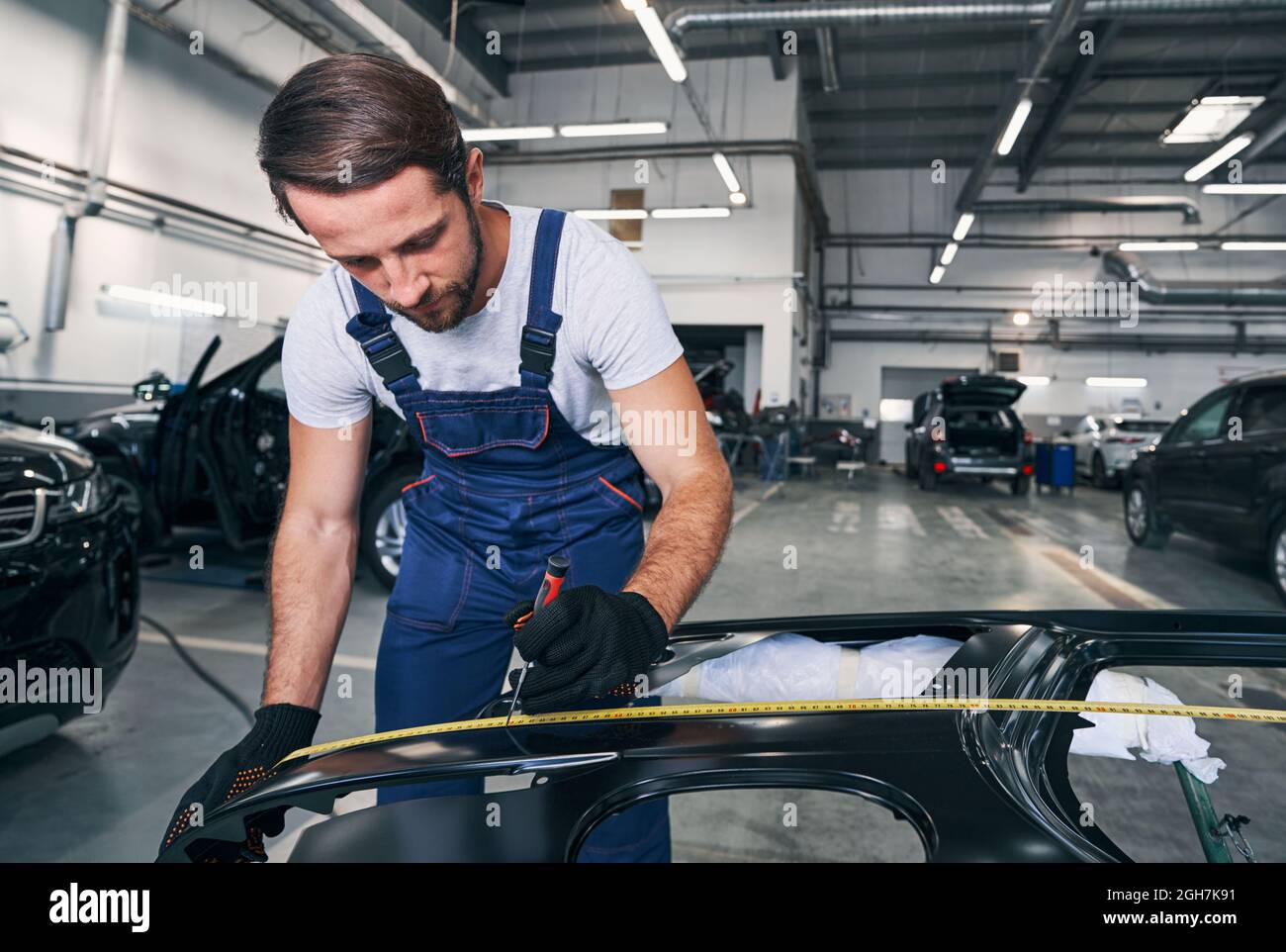 Male auto mechanic making length mark on car body Stock Photo