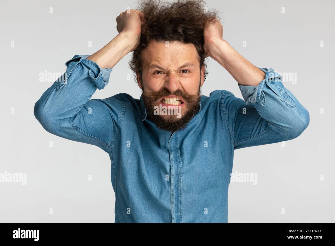 angry bearded man in denim shirt being nervous and pulling hair out