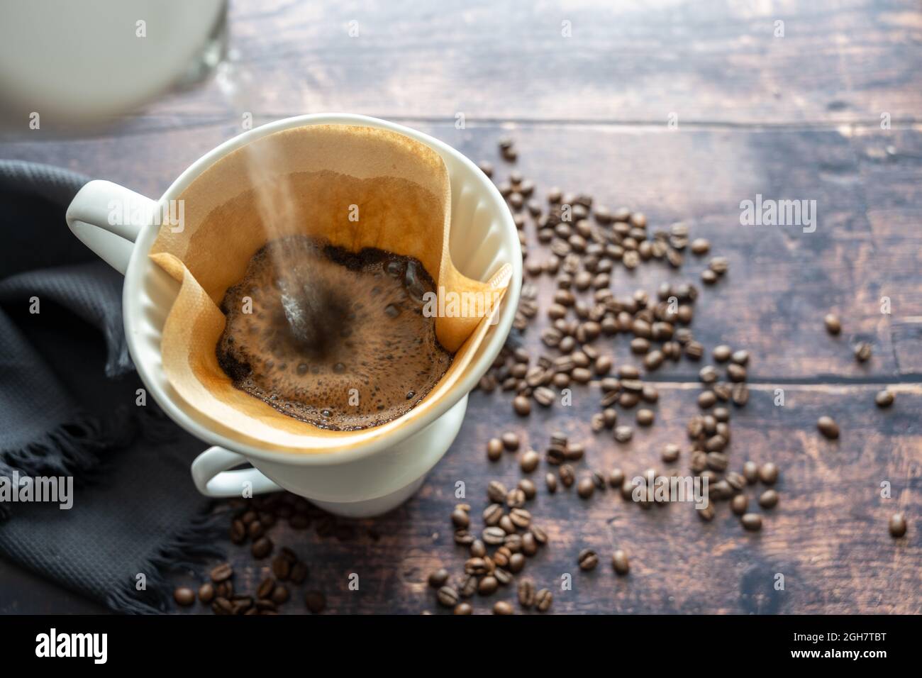 Pouring boiling water on ground coffee in a paper filter and a porcelain holder on a mug for an aromatic brewed hot drink, rustic wooden table with so Stock Photo