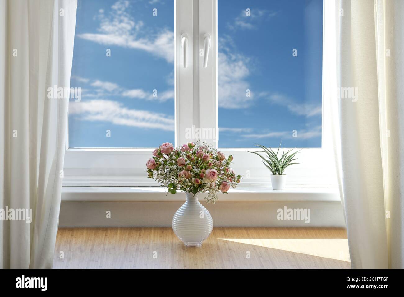 romantic flower bouquet with roses and baby's breath in a white vase on a table by the window with blue sky and clouds, copy space, selected focus Stock Photo