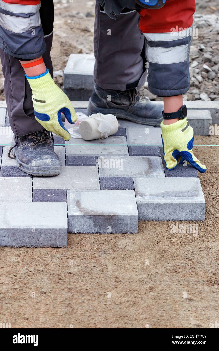 Paving Thread A worker in light green work gloves is laying paving slabs under the ...