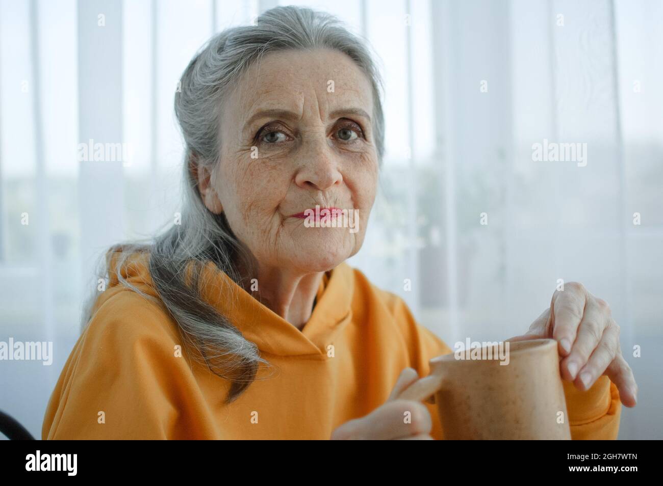 Dreamy eccentric middle aged woman sitting with cup of black tea or coffee, looking at camera. Peaceful mature lady enjoying no stress calm positive Stock Photo