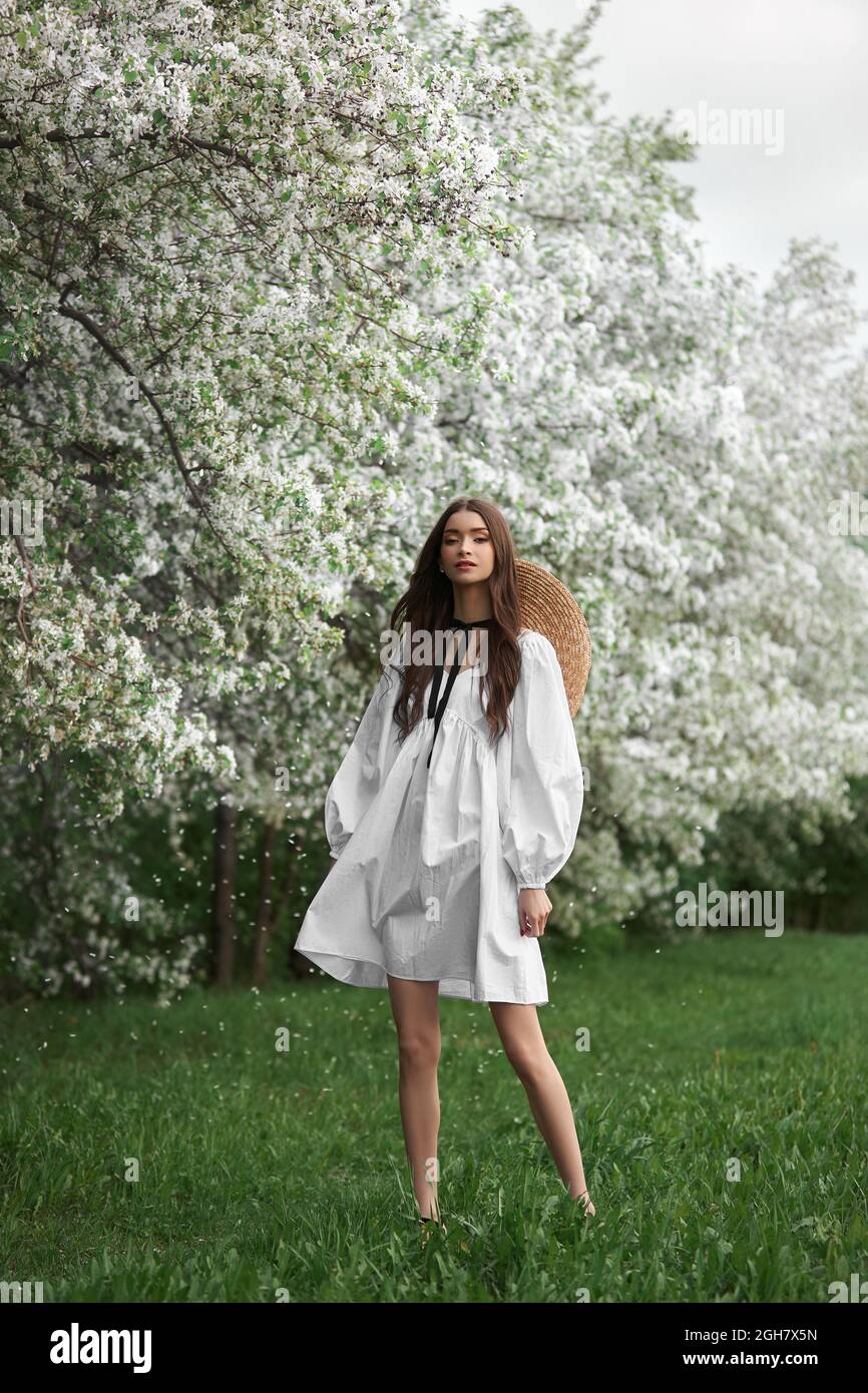 Young woman in white dress with a straw hat walks through blooming ...