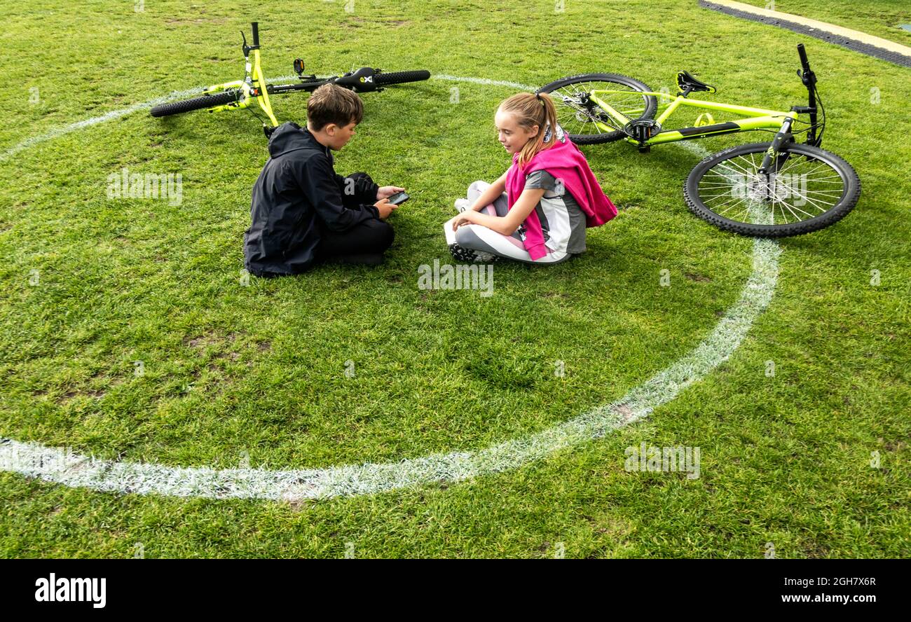 Preteen boy and girl resting from a bicycle ride in the park area of Liverpool One Stock Photo