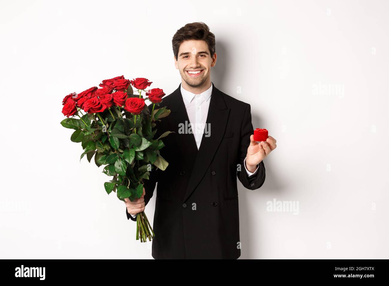 Image of handsome man in black suit, holding bouquet of red roses and a ...
