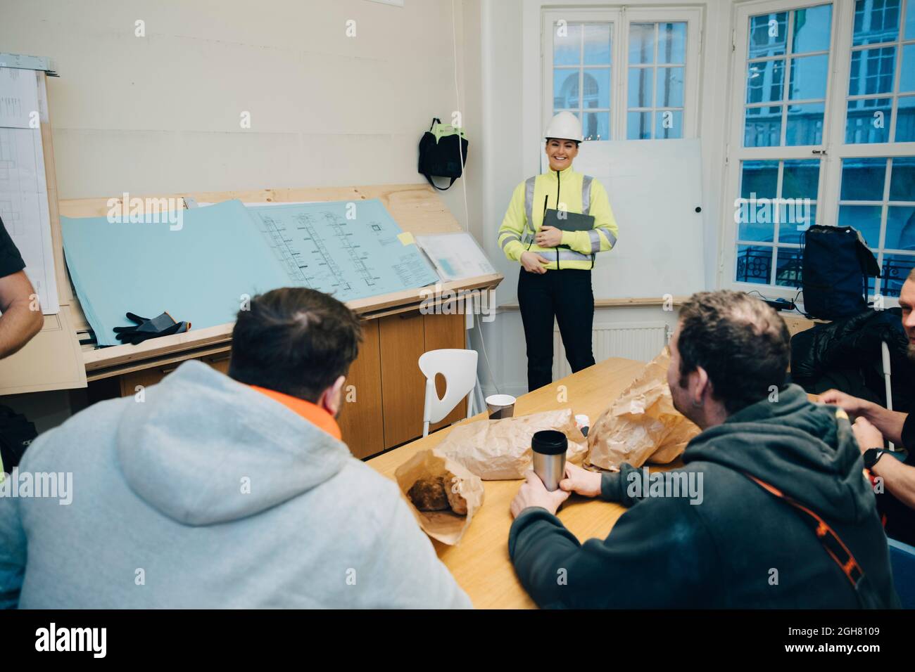Smiling female engineer discussing with male construction workers in office Stock Photo