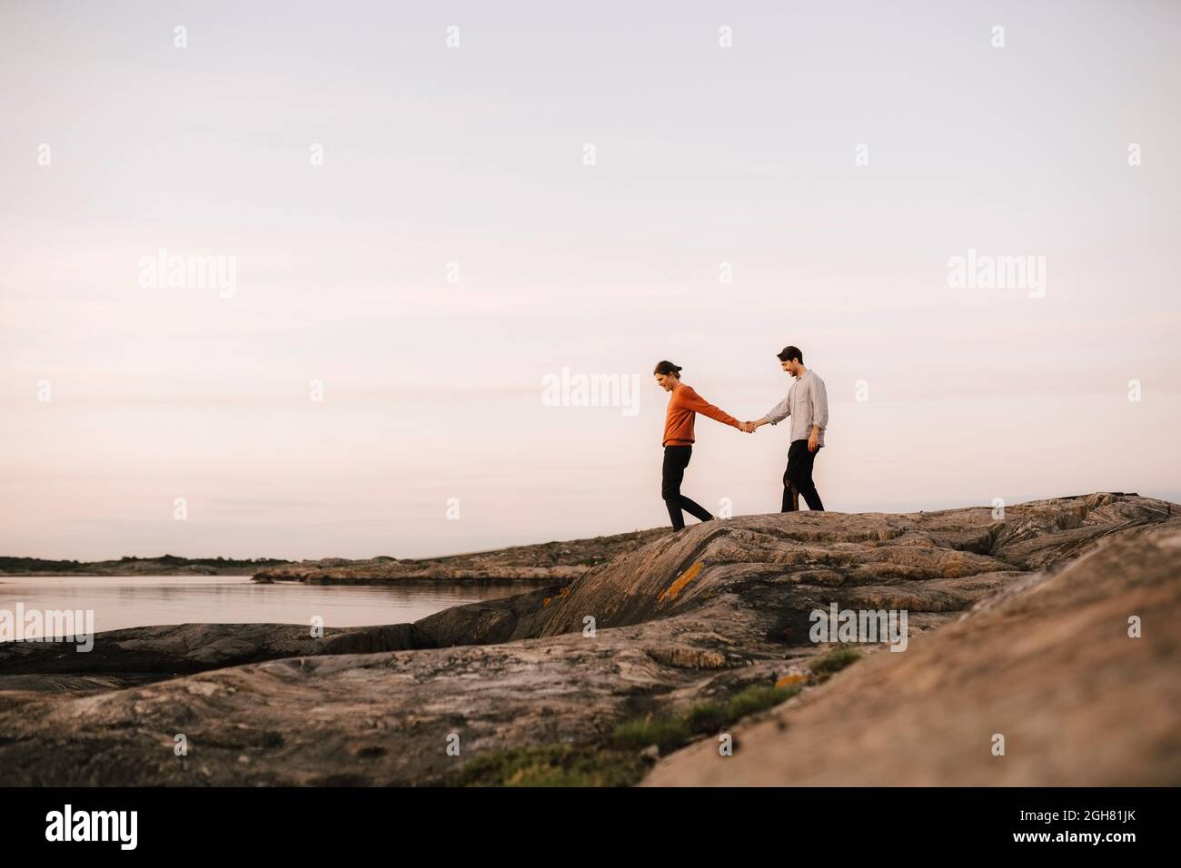 Gay couple holding hands while walking at lakeshore against sky Stock Photo