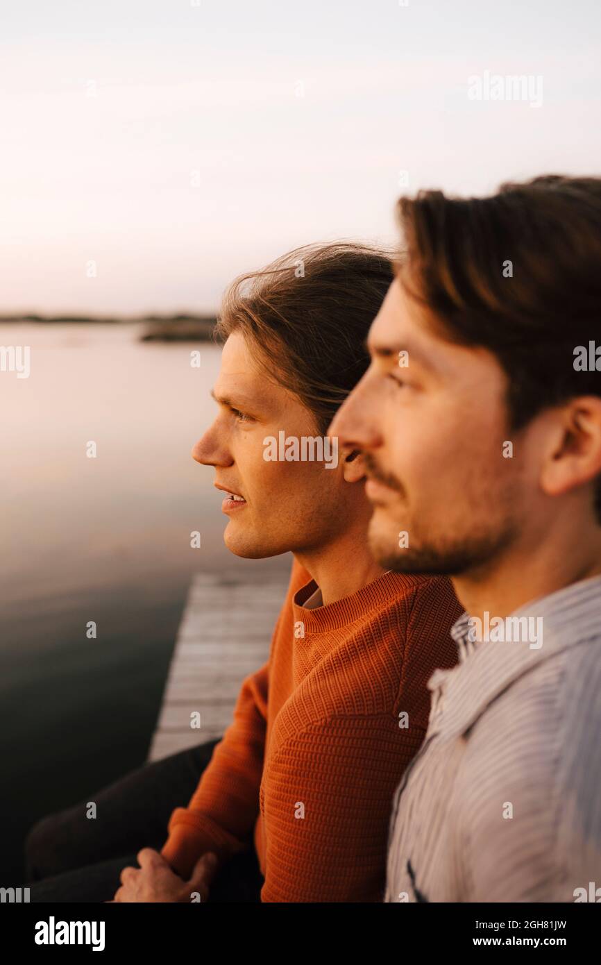 Gay couple looking away while spending leisure time at lakeshore Stock Photo