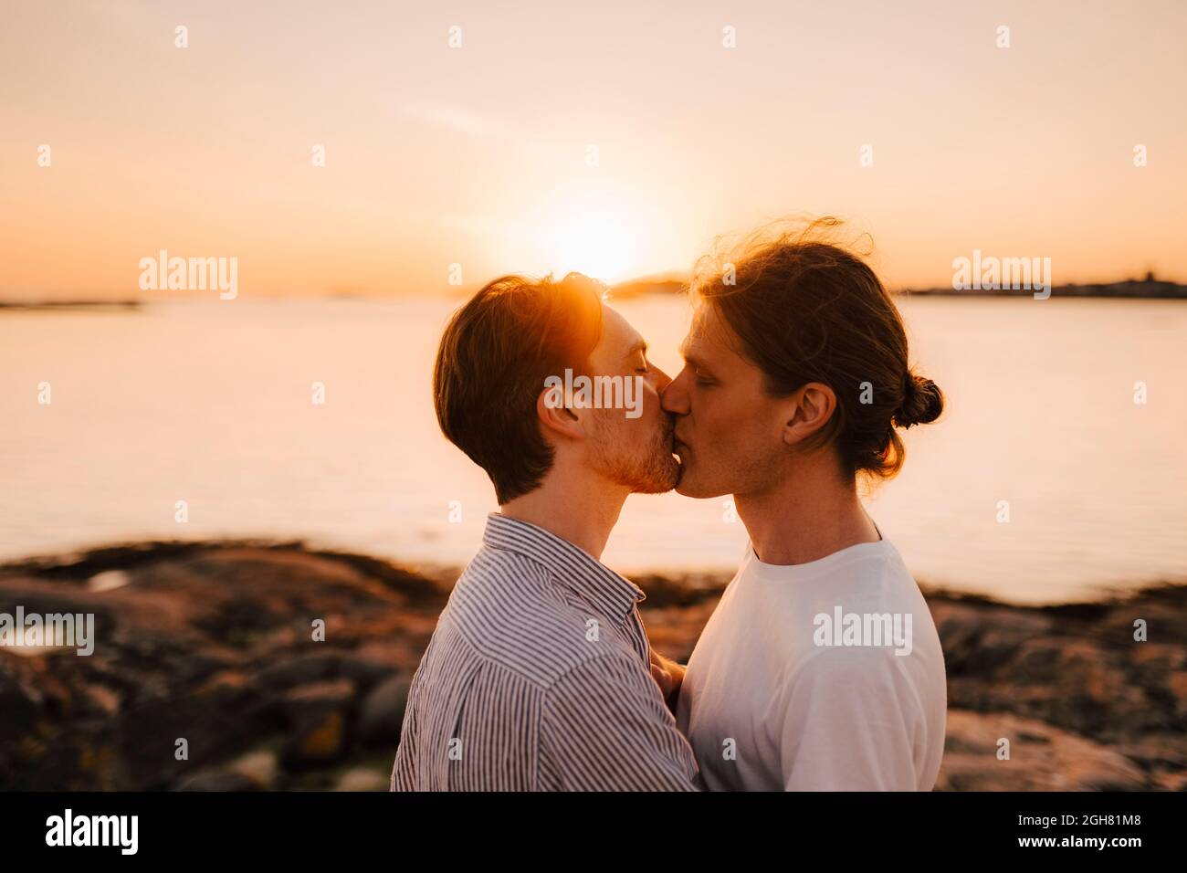 Male friends lip kissing at lakeshore during vacation Stock Photo