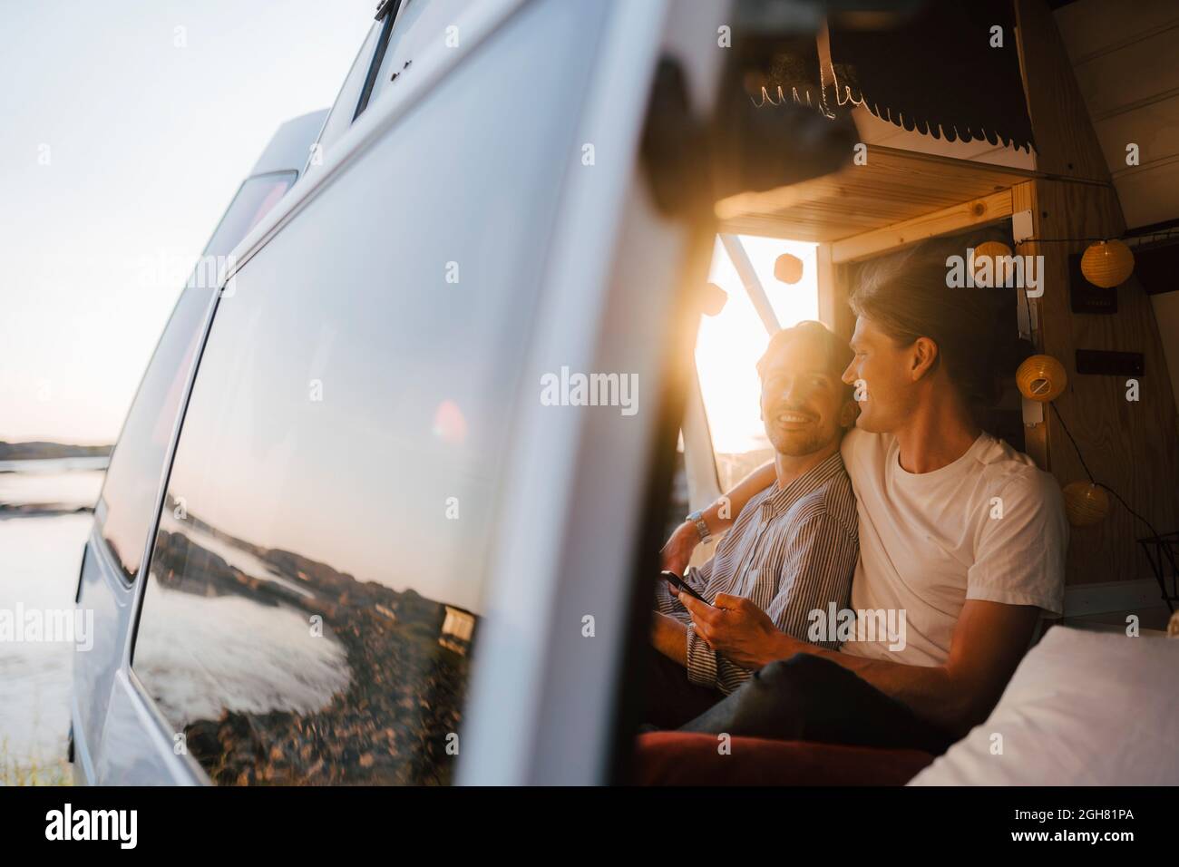 Man with arm around of boyfriend sitting at motor home in evening Stock Photo