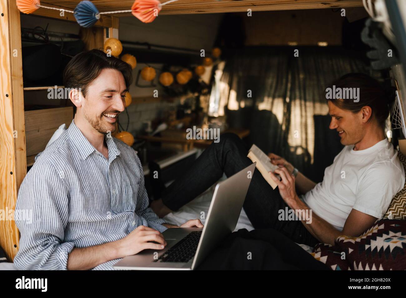 Smiling man using laptop sitting by boyfriend in camping van Stock Photo