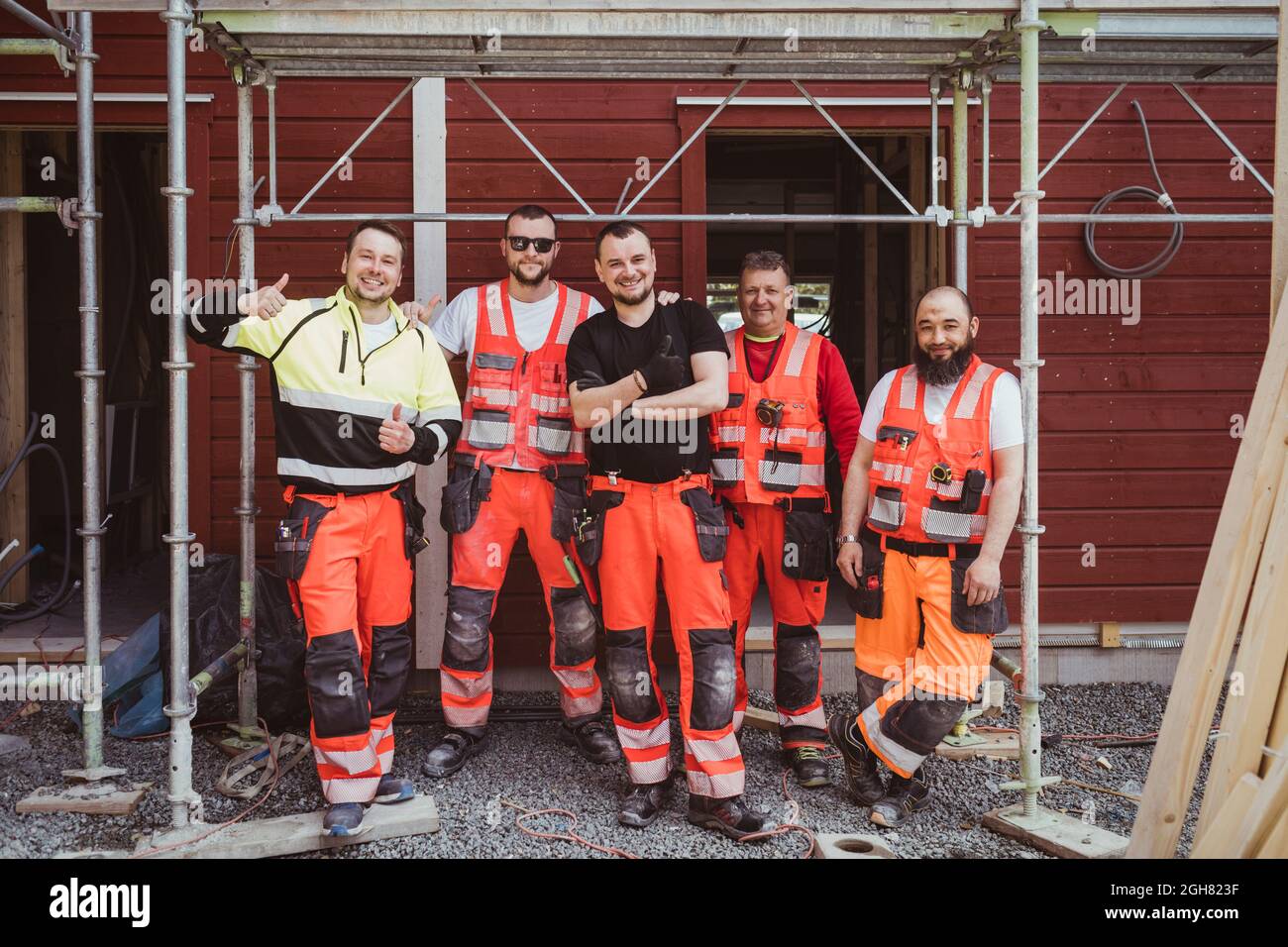 Full length of smiling male construction workers standing together at site Stock Photo