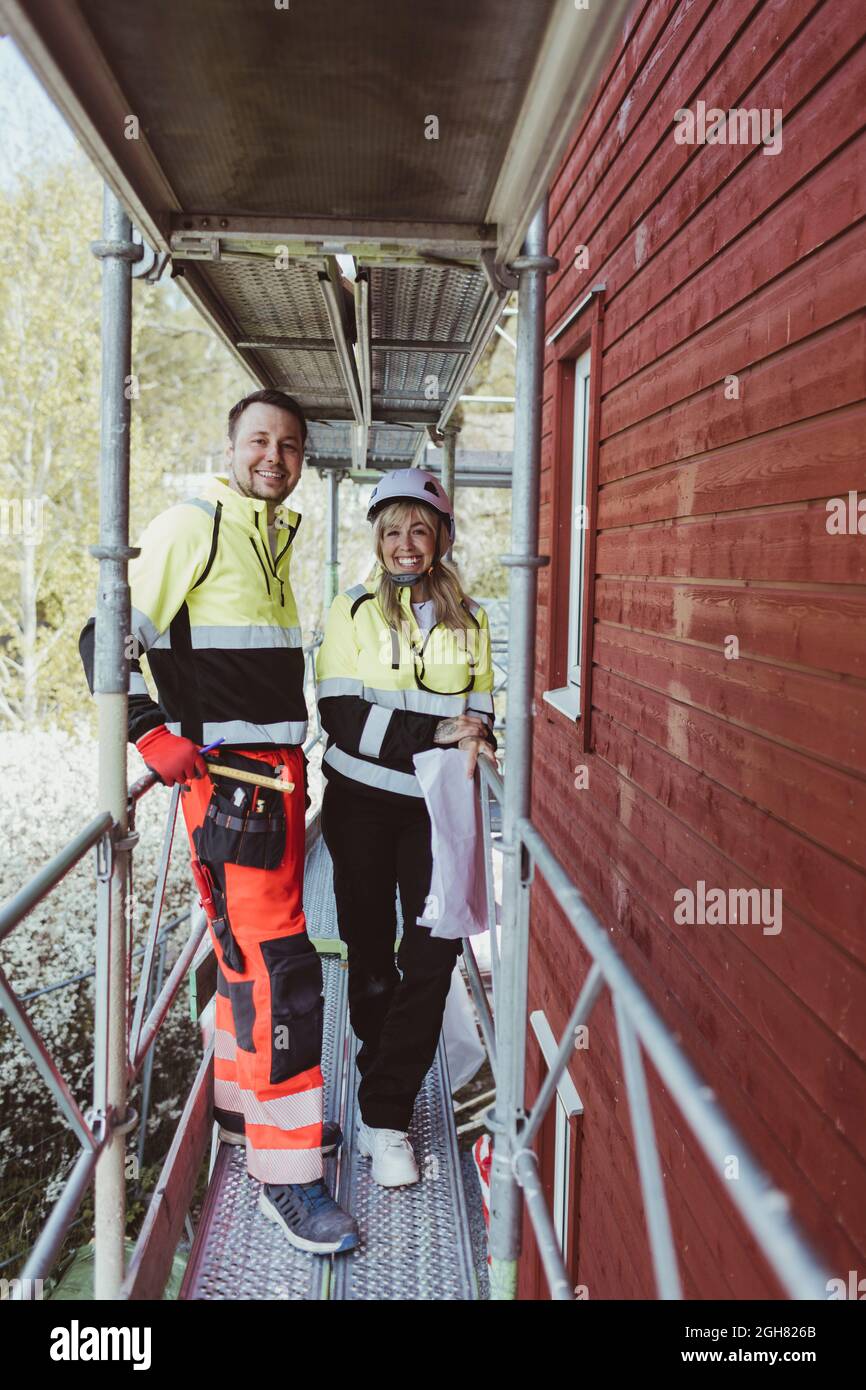 Full length of happy male construction worker with female colleague standing at scaffolding Stock Photo