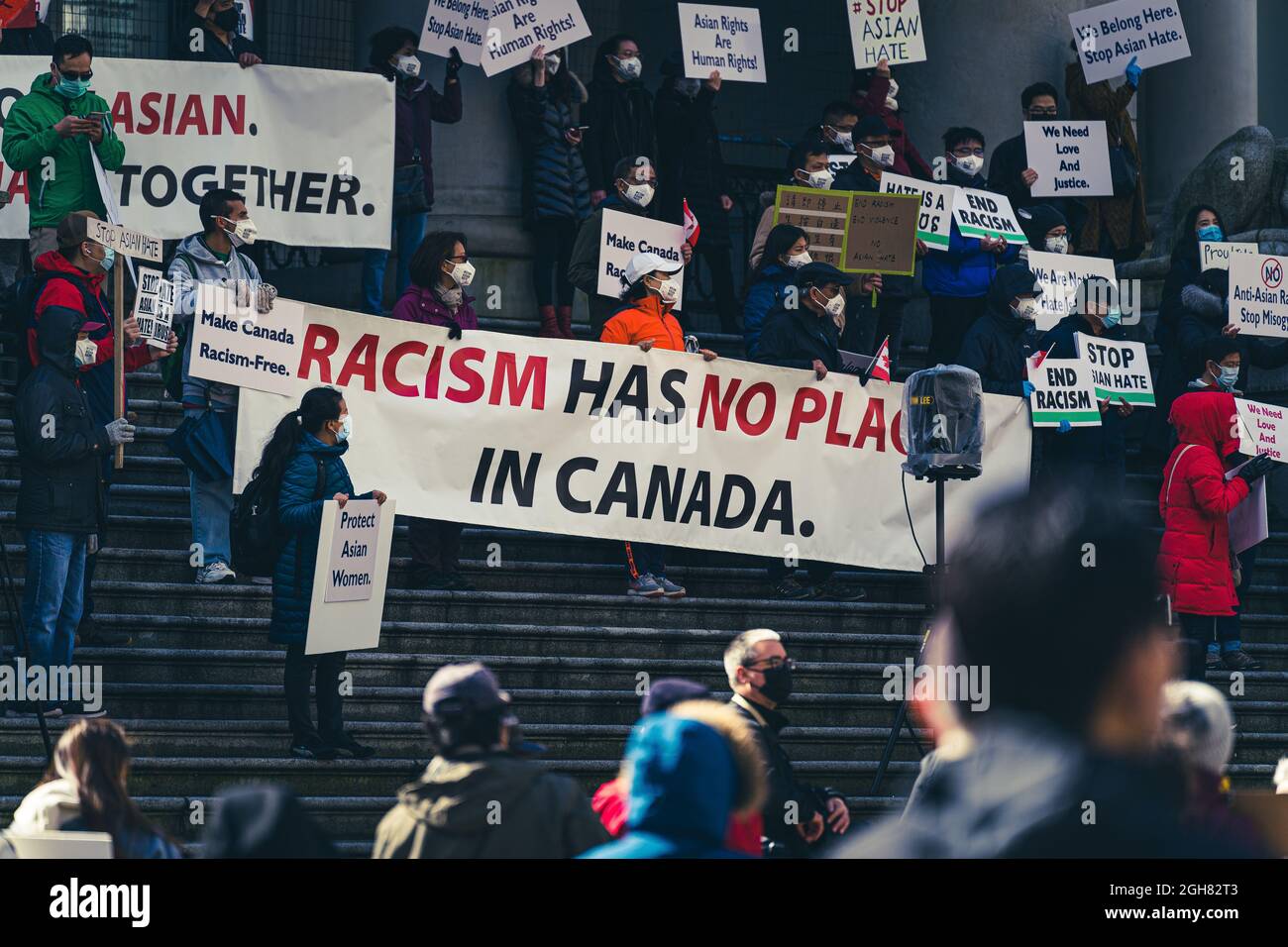 VANCOUVER, CANADA - Apr 12, 2021: The people on steps holding up a sign Racism has no place in Canada Stock Photo