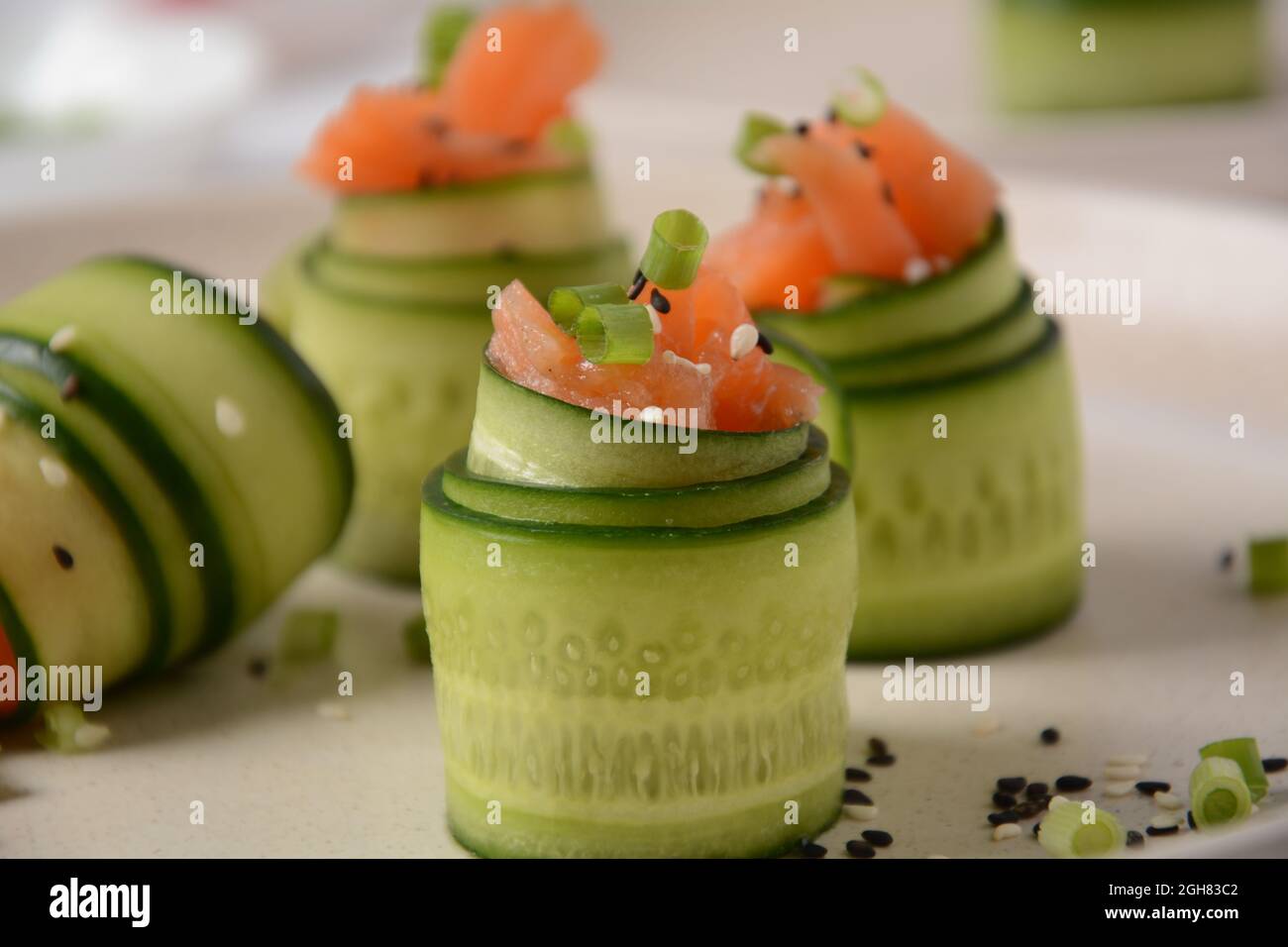 Cucumber rolls with pieces of salted salmon, black and white sesame seeds, chopped green onion. Holiday vegetable appetizers Stock Photo