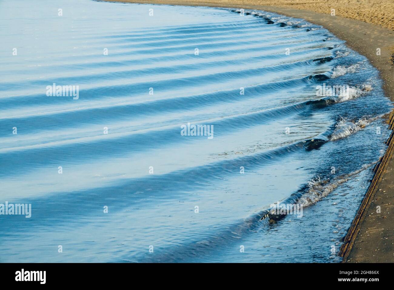 Small waves gently rolling in succession on the seashore at sunrise Stock Photo