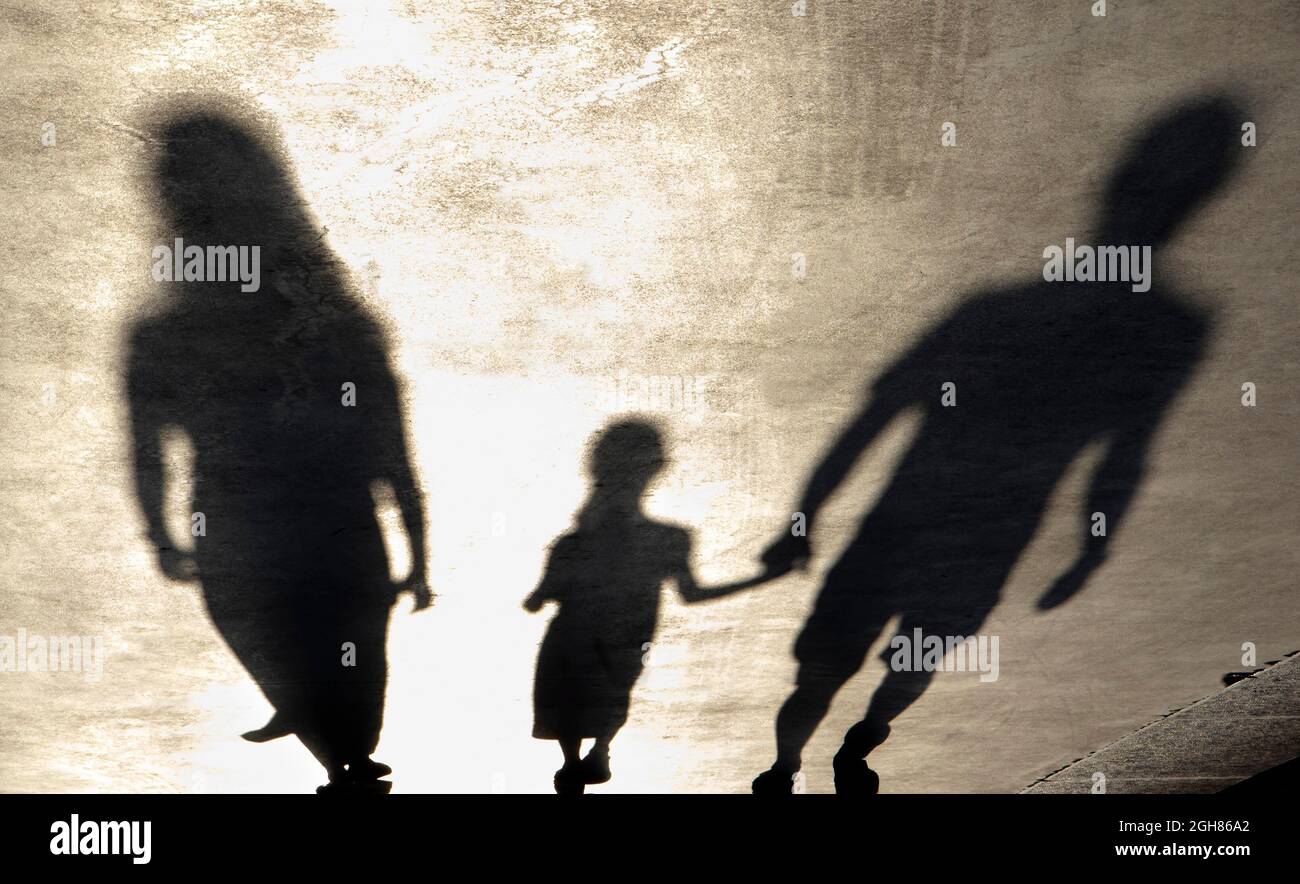 Blurry shadow silhouette of a family walking on a promenade on a summer day, in sepia black and white Stock Photo