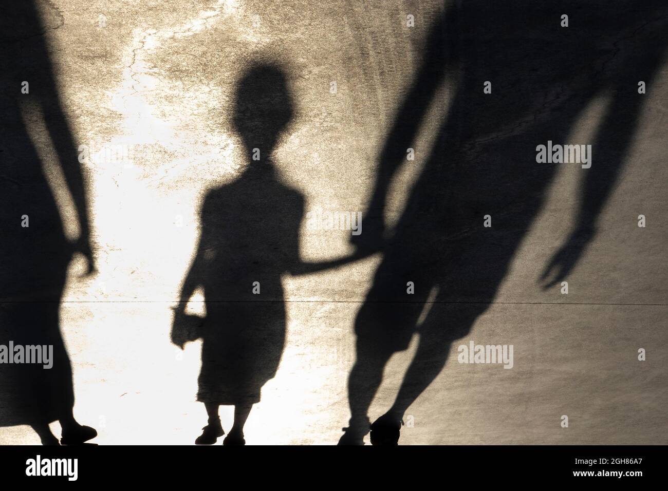 Blurry shadow silhouette of a little girl walking hand in hand with a father on a promenade on a summer day, in sepia black and white Stock Photo