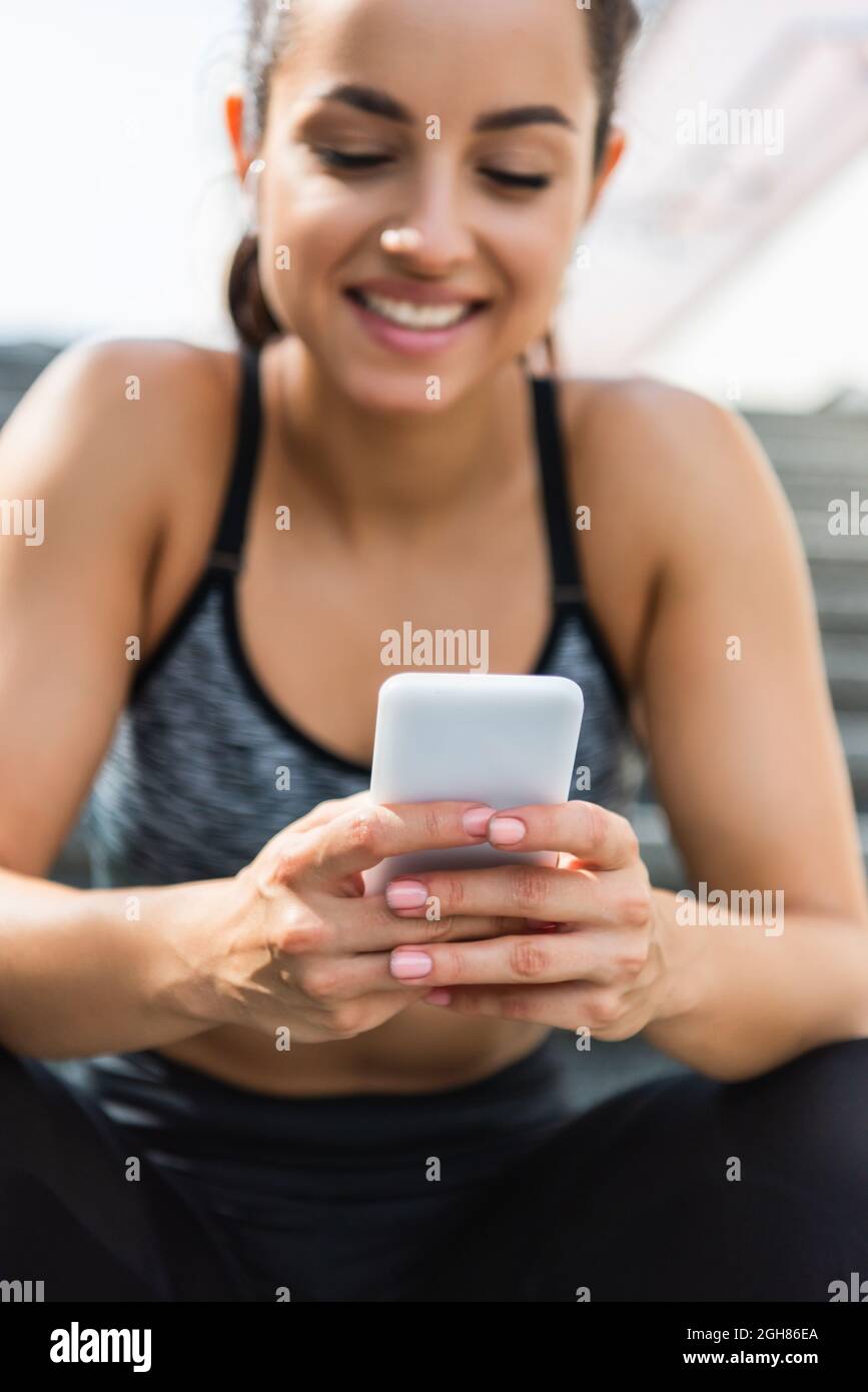 blurred and smiling sportswoman using smartphone outside Stock Photo