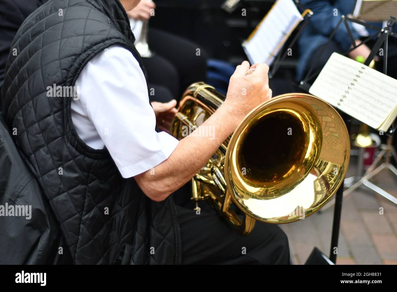 A live street band, a view of a brass instrument, French horn sitting on a mans lap Stock Photo
