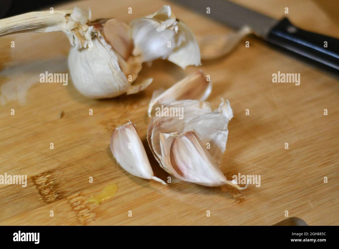 Freshly cut garlic cloves, allium sativum, as they have been extracted from the bulb, sliced on a wooden bread board in a domestic kitchen Stock Photo
